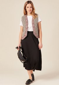Gilet a fantasia floreale con rifiniture rosse, t-shirt bianca, gonna plissè nera e mocassini neri. Abbinato con una borsa nera a tracolla.