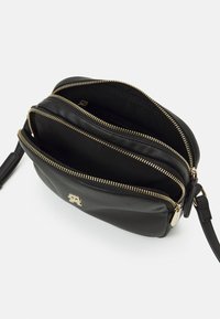 Borsa a tracolla nera in pelle con zip dorate. Caratterizzata da tre scomparti e un piccolo logo. Texture liscia e forma arrotondata.