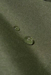 Tessuto verde impermeabile con una superficie texturizzata, con due gocce d'acqua che si posano su di esso, evidenziando le sue proprietà repellenti per l'acqua.