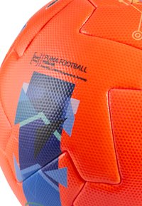 Balón de fútbol naranja con superficie texturizada, con patrones geométricos en azul y negro. Marcado con "PUMA FOOTBALL" y fabricado con material libre de PVC.
