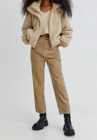 Beige sherpa jacket with a collared neckline, paired with beige corduroy trousers. Black chunky boots complete the outfit.