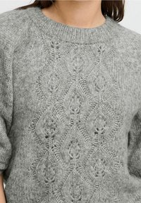 Grå stickad tröja med en texturerad diamantmönster, rund halsringning och korta ärmar. Material av mjuk ull med en mysig utseende.