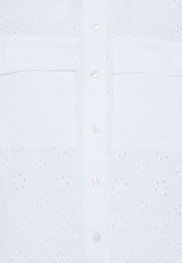 Chemise blanche à boutons avec motifs floraux ajourés et deux poches poitrine.