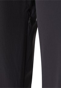 Fekete szövetnadrág közeli képével, amelyen az egyik oldalon két függőleges cipzárzseb látható.