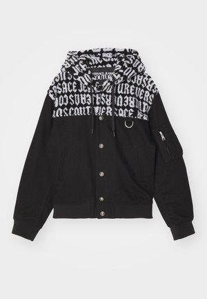 Veste bomber noire avec une capuche à motifs. Comprend des fermetures métalliques, des poches latérales et une texture de tissu combinant des matériaux lisses et pelucheux.