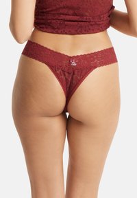 Bordeaux kanten slipje met geschulpte afwerking, met een bloemmotief en een doorzichtige textuur. Ontworpen voor minimale bedekking en comfort.