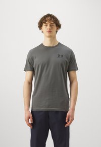 T-shirt gris à manches courtes avec col rond, arborant un petit logo noir sur la poitrine. Le matériau semble doux et décontracté.