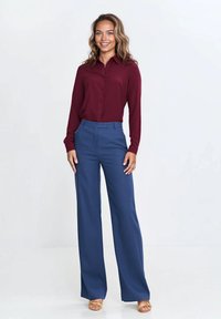 Burgundowa koszula z guzikami zestawiona z granatowymi, szerokimi spodniami z wysokim stanem. Gładki materiał z dopasowanym krojem i klasycznym kołnierzykiem.