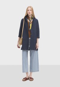 Námořnický dlouhý kabát, béžový top, proužkované široké kalhoty, hnědé sandály s přezkou. Šátek s modrými a žlutými akcenty. Hladká tkanina, uvolněný střih.