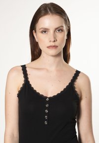 Top nero senza maniche con pizzo lungo il collo e le aperture delle maniche, caratterizzato da una patta di bottoni al centro con tre bottoni circolari in argento.