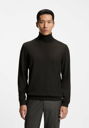 Schwarzer Rollkragenpullover aus weichem Strickmaterial, mit langen Ärmeln und gerippten Bündchen, kombiniert mit gemusterten grauen Hosen.