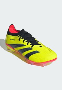 Crampons de football jaunes avec des rayures et des lacets noirs, présentant une tige texturée et des accents roses sur la semelle et le col intérieur.