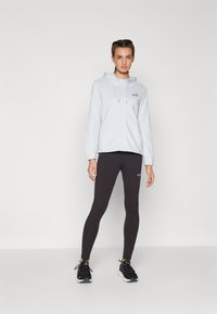 Šviesiai mėlyna zip-up gobtuvė su subtiliu logotipu, derinama su juodais leggingais. Ypatybės: laisvas kirpimas ir sportinė dizaino, papildyta juodomis sportinėmis bateliais.