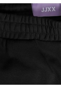 Black cotton jogger waistband with gathered elastic detail. Features a purple label with "JJXX" in white text. Smooth fabric texture.