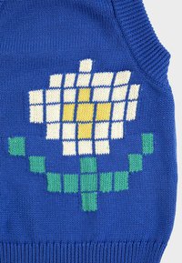 Chaleco de punto azul con un diseño pixelado de una flor blanca y amarilla con tallo y hojas verdes en el frente.