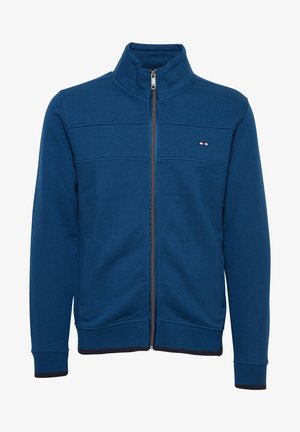 Giacca blu con zip realizzata in tessuto morbido, dotata di colletto alto, cuciture verticali e un piccolo logo sul lato sinistro del petto. Polsini a coste blu navy.