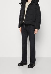 Svart puffjacka med huva, beige t-shirt, mörka jeans och kraftiga svarta kängor. Slät textur och enkel design.