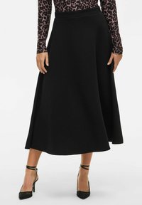Černá áčková sukně s hladkou texturou, vysokým pasem a splývavou siluetou, v kombinaci s černými lodičkami s špičatou špičkou.