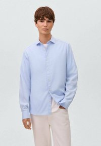 Camicia azzurra chiara button-up con maniche lunghe, colletto a punta e una trama liscia, indossata sopra una maglietta bianca.