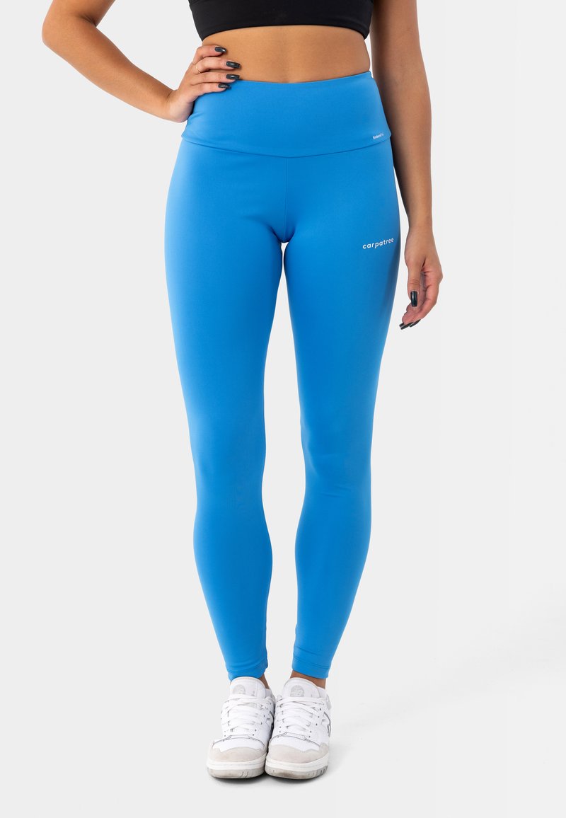 Leggings blu a vita alta realizzati in materiale elastico, con una texture liscia e un piccolo logo sulla coscia. Indossati con sneakers bianche.