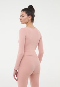 Dopasowany top z długim rękawem i pasujące legginsy w miękkim, jasnoróżowym prążkowanym materiale. Gładka faktura, okrągły dekolt oraz widoczne stebnowane szwy.
