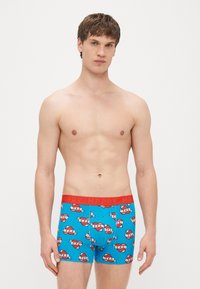 Zilas bokseršorti ar sarkanu jostasvietu, uz kuras rakstīts vārds "LAIMĪGS." Dizains ietver atkārtotus sirds un lentu rakstus ar tekstu "TĒTIS."