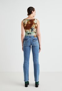 Prilegajoča majica brez rokavov z barvnim vzorcem v zemeljskih tonih, v kombinaciji z modrimi ozkimi jeans hlačami, ki imajo oznako na žepu in okrasno šivanje na žepih.