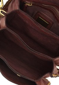 Interno di una borsa in pelle marrone con texture in suede, caratterizzato da due scomparti, una cerniera dorata e una piccola etichetta di tessuto all'interno.