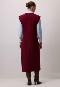 Pikk burgundi värvi ilma varrukateta kleit sirge lõikega, millel on seljaõmblus, kantud helesinise särk üle ja kombineeritud pruuni põlvekõrguste saapadega.