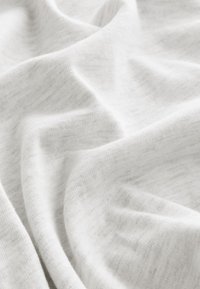 Tissu tricoté blanc doux avec de délicats plis et une surface lisse légèrement texturée, suggérant un matériau léger.