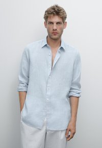 Chemise en lin bleu clair avec un devant à boutons, des manches retroussées et une coupe décontractée. Conçue avec un col classique et une texture douce.