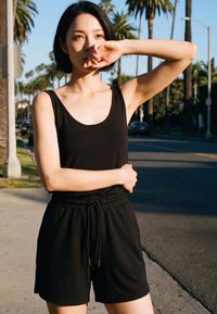 Noor naine musta topi ja lühikeste pükstega varjab päikesevalguse eest silmi, seistes päevasel ajal palmioksadest ääristatud tänaval.