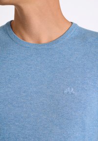 Vaaleansininen neulepaita, jossa on pyöreä kaula-aukko ja resorikireät hihansuut. Rinnassa hienovarainen brodeerattu logo. Pehmeä pinta.