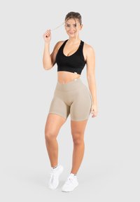 Zwart geribbeld crop top met een ronde halslijn, gecombineerd met beige high-waisted shorts. Model draagt witte sneakers met zwarte accenten.