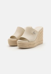 Sandalias de cuña beige con diseño de punta abierta, hechas de tela, con una media suela de yute trenzado y un pequeño acento metálico con el logo.