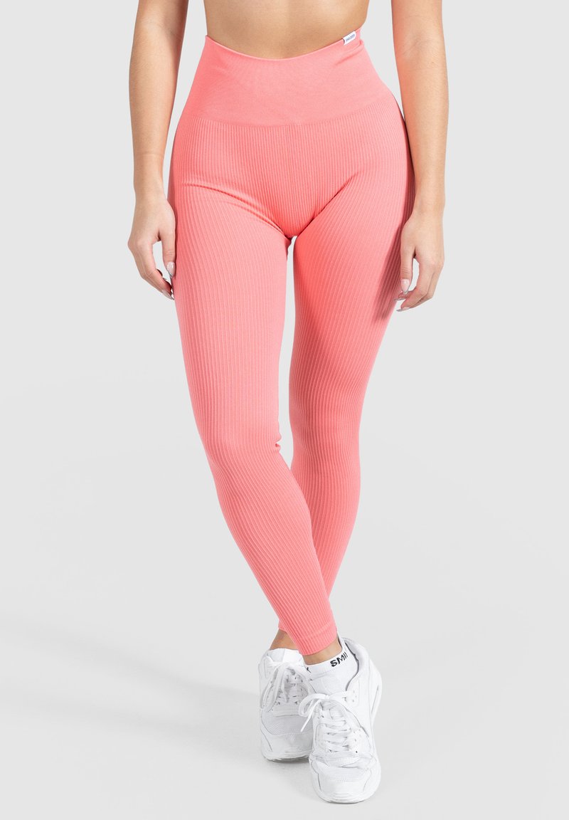 Leggings rosas acanalados con un diseño de cintura alta, que presentan una textura suave y un ajuste ceñido, combinados con zapatillas deportivas blancas.