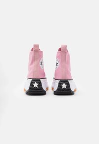 Pink canvas ankle boots with a black sole, white star accent on the heel, and a circular logo detail on the outer side.