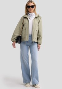 Svetlozeleni zip-up jopič z elastičnimi manšeti, bela majica, svetlo modri široki jeans, črna torbica in sončna očala. Bela šal s patternom.