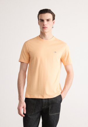 Korte mouwen oranje katoenen t-shirt met een ronde hals; heeft een klein logo op de borst; gecombineerd met donkere jeans.