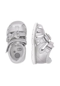 Sandales pour tout-petits argentées avec un nœud, des sangles en Velcro, un design ouvert et des surfaces texturées. Semelle blanche avec des motifs de traction et semelles intérieures rembourrées.