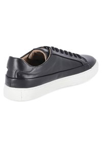 Black leather sneaker with a white rubber sole, featuring a smooth texture, rounded toe, and contrasting stitching along the sides.