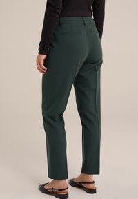 Gröna skräddarsydda byxor i ett mjukt tyg, med rak benform, två bakfickor och platt frontdesign. Svarta sandaler synliga.