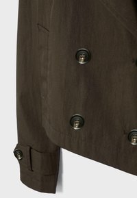 Dark brown jacket sleeve and lower front with black buttons and a cuff strap, showing pocket detail and stitching.