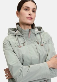 Light green waterproof jacket with a hood, featuring zippered front, adjustable drawstrings, and contrasting stitching details.