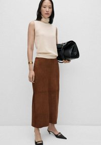 Beige mouwloze coltrui, bruine suède midi-rok, zwarte leren handtas en zwarte puntige hakken. Effen achtergrond.