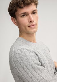 Grauer gestrickter Pullover mit einem Kabelmuster, rundem Ausschnitt und strukturiertem Stoff. Die Passform ist körpernah, mit Rippdetail.