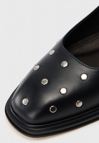 Sapatos de couro pretos com um design de biqueira quadrada, adornados com tachas prateadas distribuídas uniformemente ao longo da superfície superior. Textura suave e estilo minimalista.