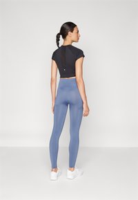 Čierny krátky top s krátkymi rukávmi, so sieťovaným detailom na chrbte. Svetlomodré legíny s vysokým pásom, hladká textúra, spárované s bielymi topánkami.