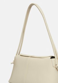 Beżowa skórzana torebka o wyraźnie zdefiniowanym kształcie, z podwójnymi cienkimi ramiączkami i zapięciem na klapkę. Gładka tekstura z subtelnymi detalami wystębnowania.