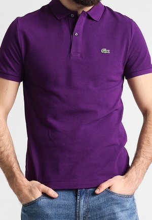 Fioletowa koszulka polo wykonana z bawełny, z kołnierzykiem, krótkimi rękawami i małym zielonym logo krokodyla na lewej piersi. Casualowy krój.